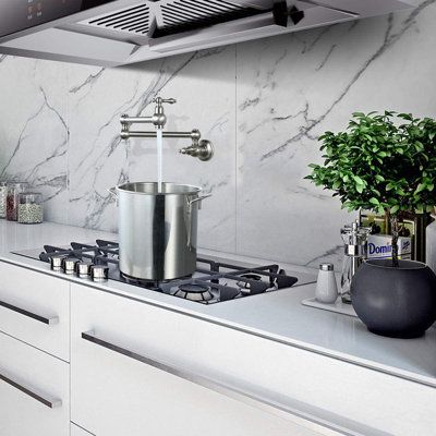 Modern kitchen with marble backsplash, pot filler faucet over stove, and a potted plant on white countertops.