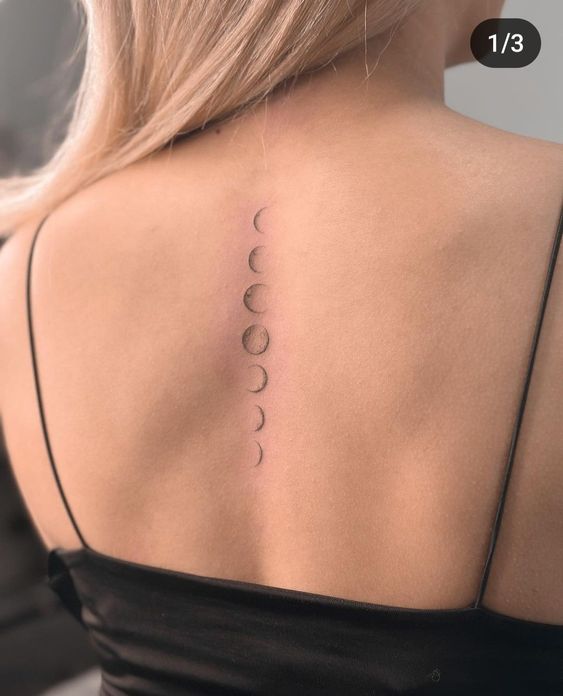 Minimalist moon phase tattoo along the spine of a woman's back, showcasing lunar cycle in a delicate design.