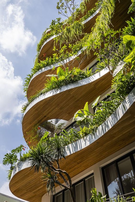 Modern building with curving balconies adorned with lush green plants, creating a unique urban garden facade.