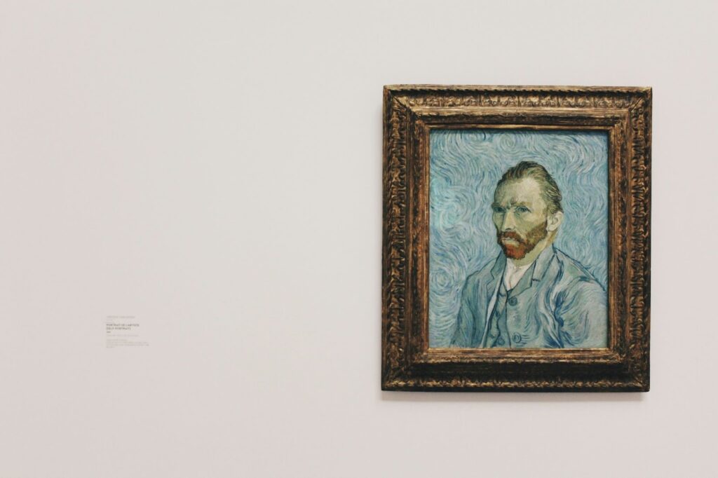 Framed painting of a bearded man against a swirling blue background, displayed on a white wall in a museum.