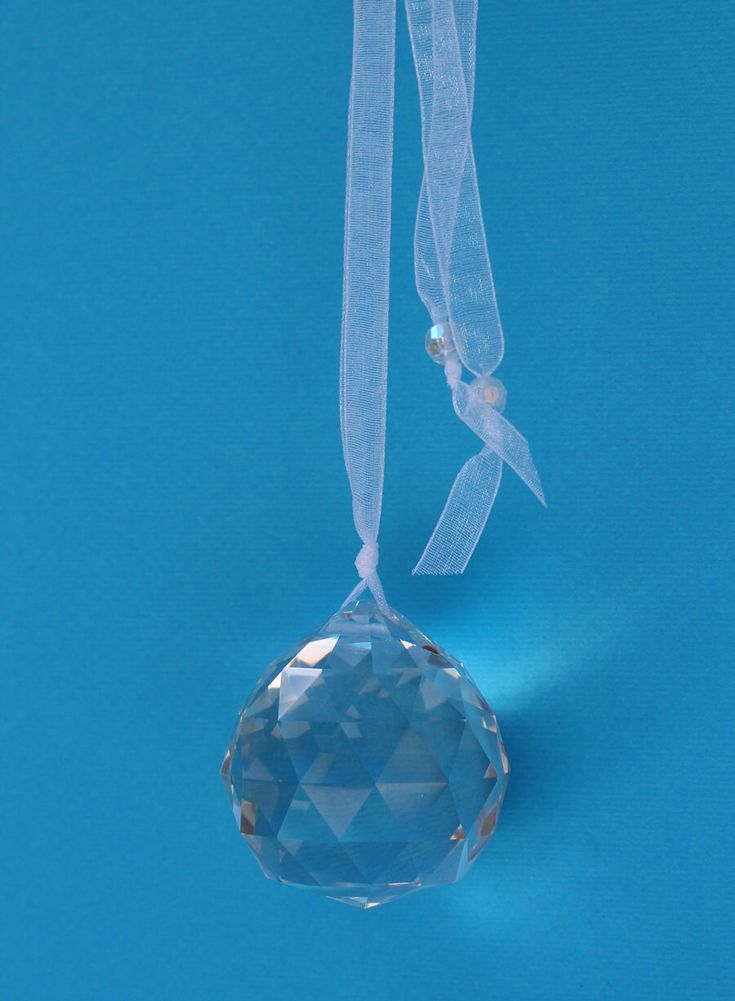 Hanging crystal prism with sheer ribbon against a blue background, reflecting light and creating a sparkling effect.