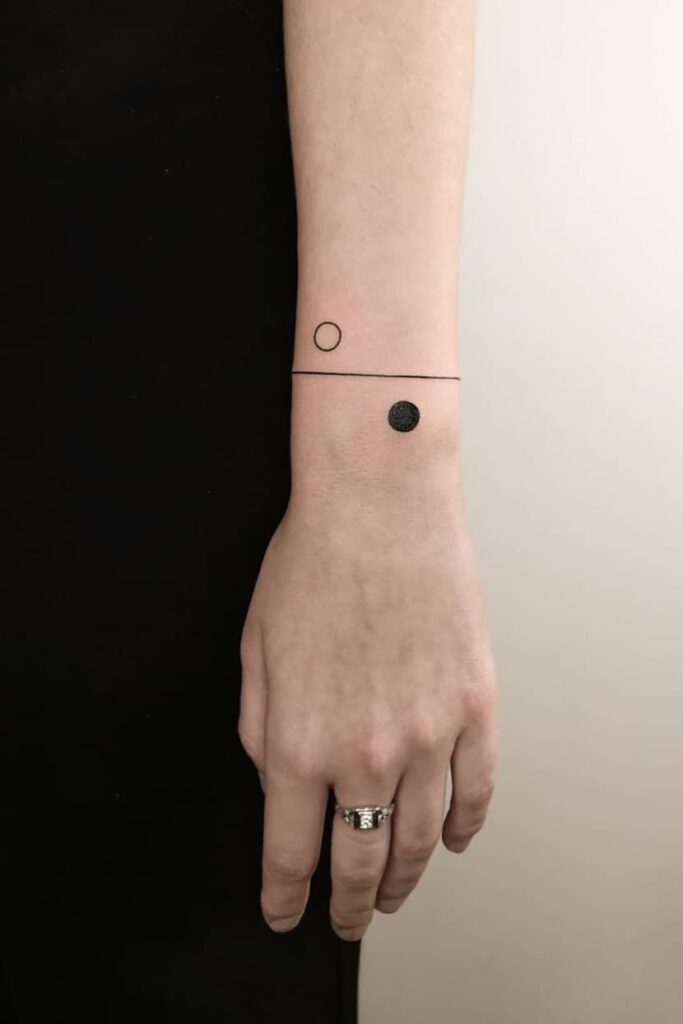 Minimalist wrist tattoo with a thin black line, an empty circle, and a filled dot, showcasing modern geometric design.