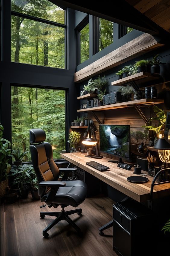 Modern home office with ergonomic chair, wooden desk, computer screen, and shelves, surrounded by large windows with forest view.