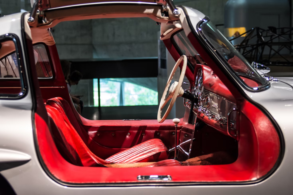 Interior of a vintage car with red leather seats and open gullwing door, showcasing a stylish design and classic steering wheel.