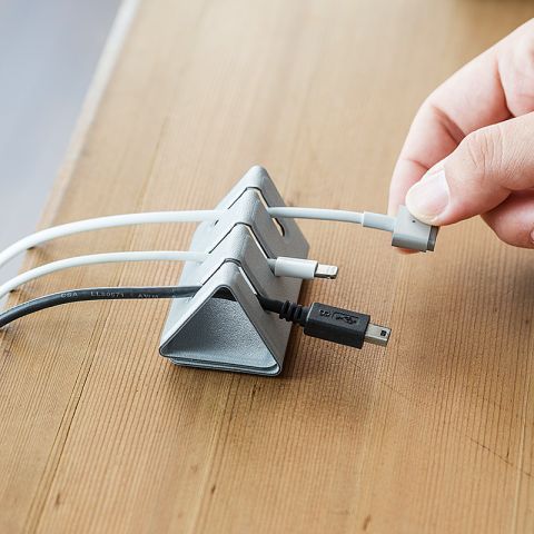 Hand organizing charging cables with a sleek desktop cable organizer stand on a wooden desk.