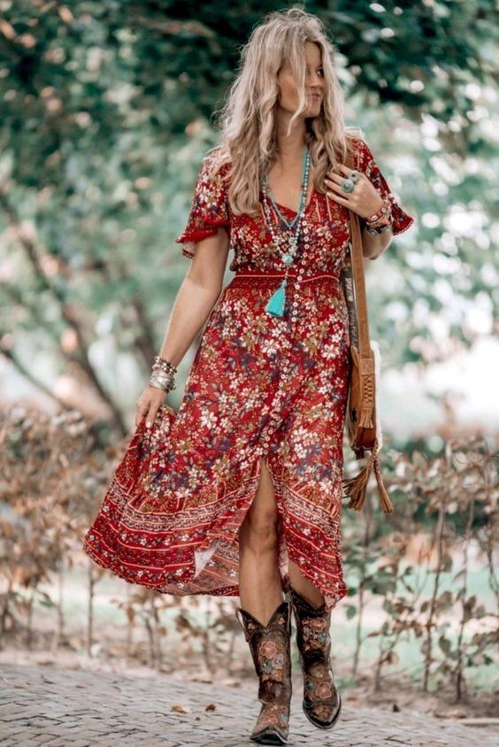 Woman in a red floral boho dress and cowboy boots walking outdoors, wearing turquoise jewelry and a crossbody bag.