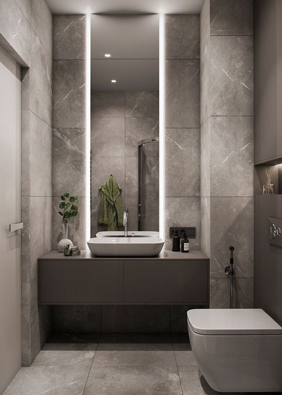 Modern bathroom with minimalist design, large mirror, illuminated vanity, and sleek fixtures in a grey color scheme.