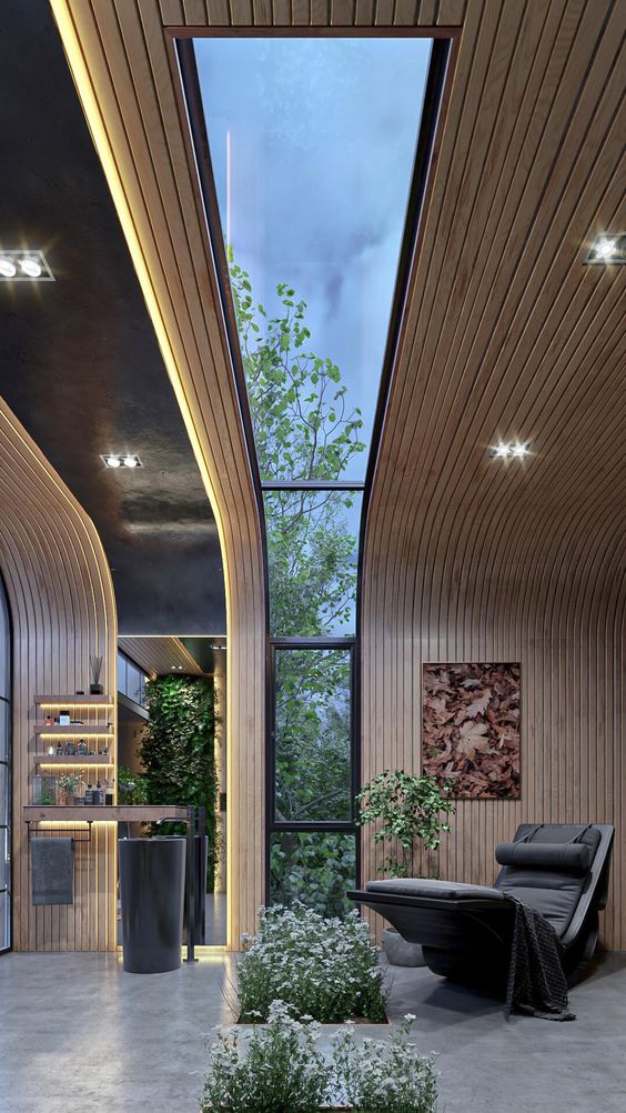 Modern interior space with wooden paneling, skylight, large windows, indoor plants, and lounge chair for relaxation.