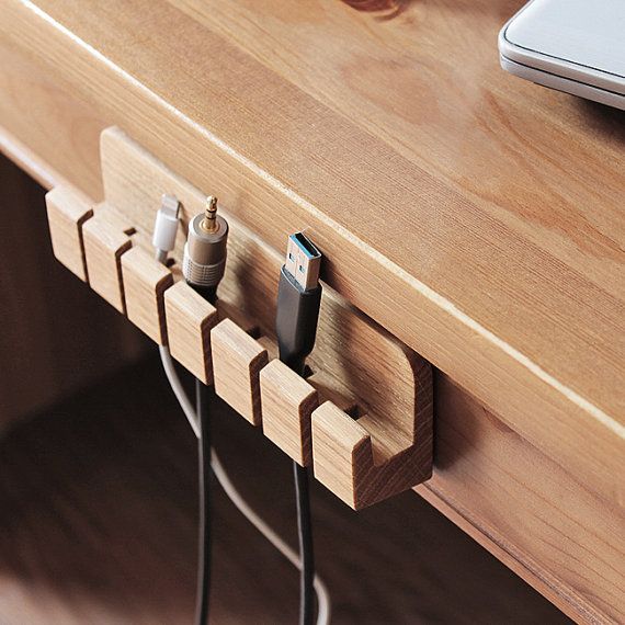 Wooden cable organizer attached to desk holding various cables neatly, promoting tidy workspace and efficient cable management.