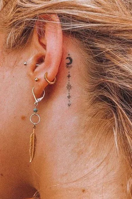 Close-up of ear piercings with gold earrings and a small moon tattoo behind the ear, featuring trendy minimalist jewelry.