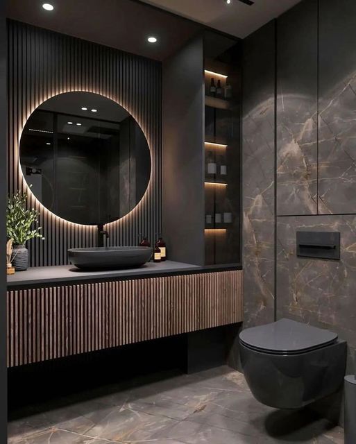 Modern bathroom with black fixtures, round backlit mirror, wooden vanity, and dark marble walls and floor. Luxurious design.