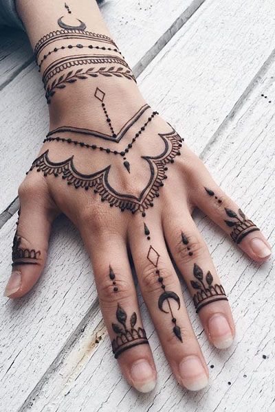 Hand adorned with intricate henna design featuring geometric patterns and floral motifs on a light wooden background.