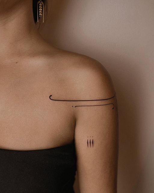 Minimalist black line tattoo on woman's shoulder and arm. Elegant modern design, wearing one earring and black top.