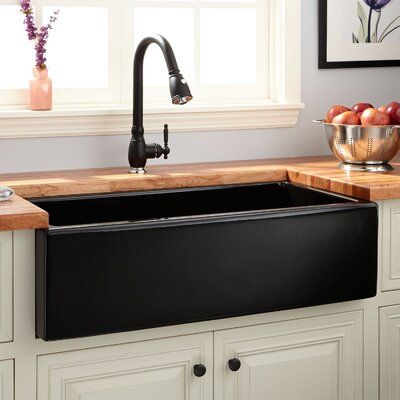 Modern black farmhouse sink with pull-down faucet, white cabinetry, wooden countertops, and a bowl of fresh apples.