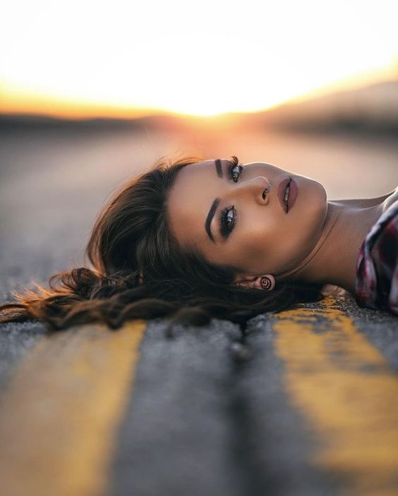 Woman lying on road with yellow dividing lines at sunset, exuding confidence and calm.