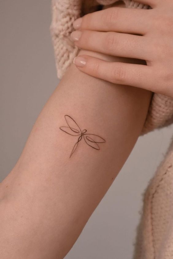 Minimalistic dragonfly tattoo on the upper arm with hand gently touching, showcasing delicate line art.
