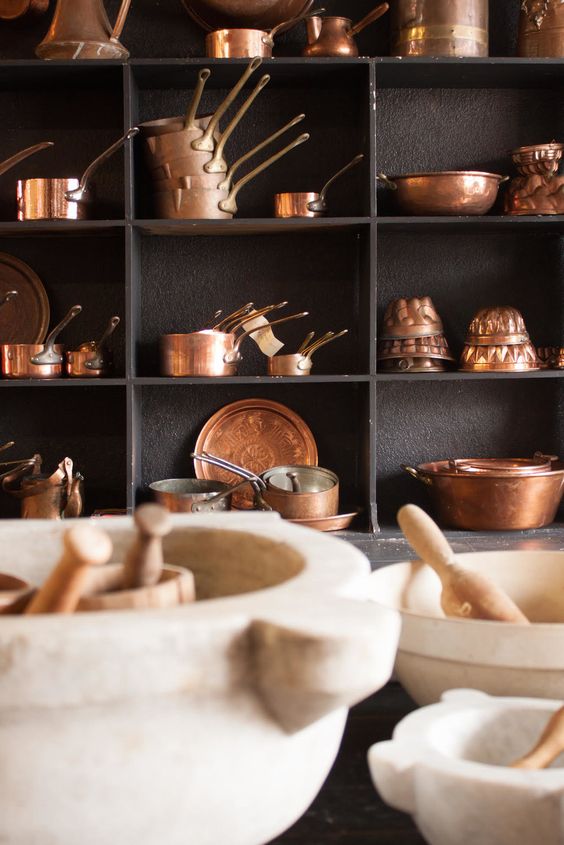 Vintage copper cookware neatly organized on black shelves, with marble mortars and pestles at the forefront.