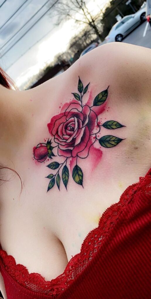 Rose tattoo on upper chest with vibrant pink petals and green leaves, enhanced by red lace top.