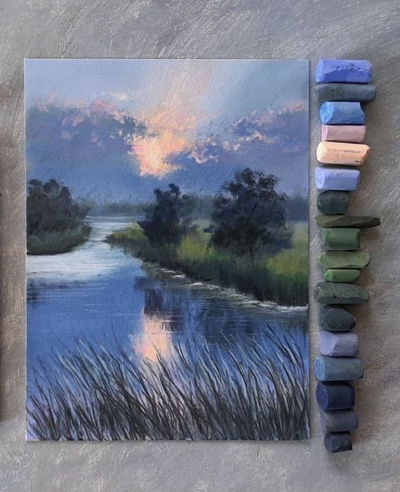 Pastel drawing of a serene river landscape at dawn, surrounded by trees, with pastel chalks in various colors beside it.