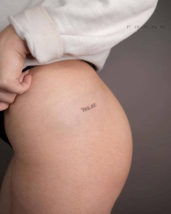 Close-up of thigh tattoo with the text Yes, sir. showcasing minimalistic ink on light skin under a white garment.