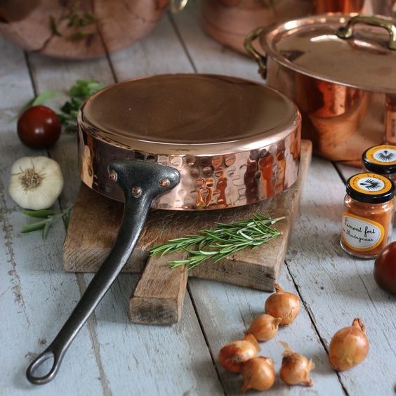 Vintage copper pan and pot with fresh ingredients like garlic, tomatoes, onions, rosemary, and spices on wooden table.