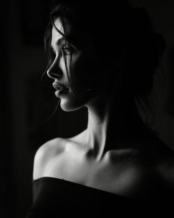 Black and white profile portrait of a woman with dramatic lighting, emphasizing the contours of her face and shoulders.