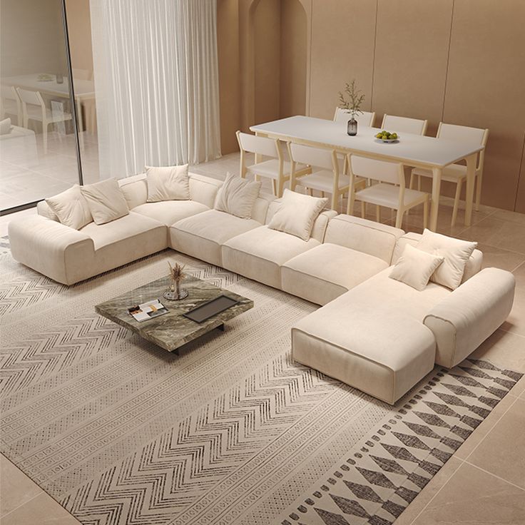 Luxurious beige sectional sofa in a modern living room, with a marble coffee table and dining area in the background.