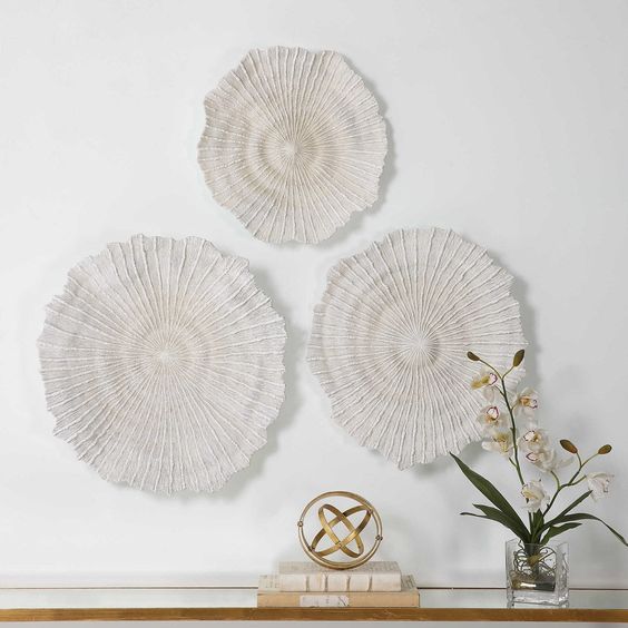 Modern wall art decor with white textured circular designs and a display with a gold geometric object and white orchid vase.