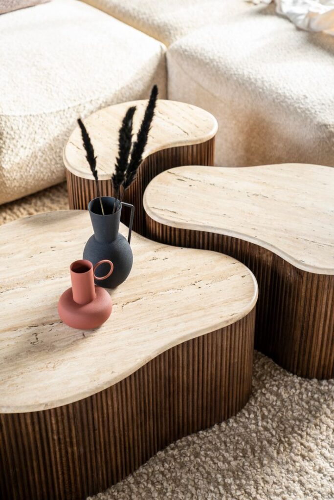 Modern coffee tables with wooden bases and cream tops, adorned with black and pink decorative vases on a cozy rug.