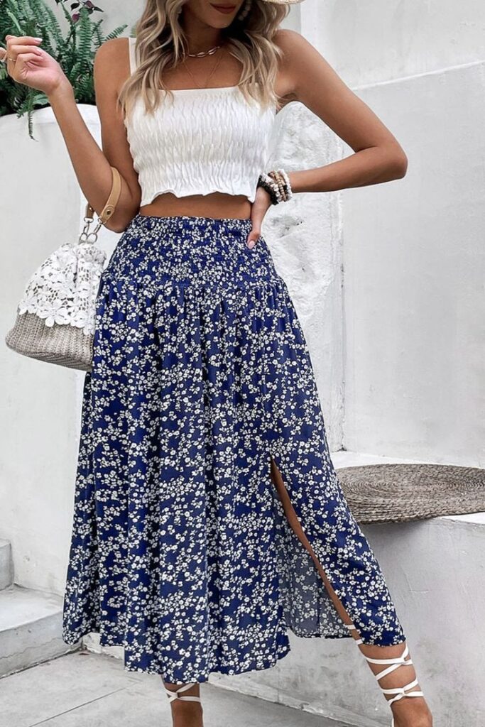 Woman in a white crop top and blue floral skirt with a slit, holding a stylish handbag, perfect summer outfit.