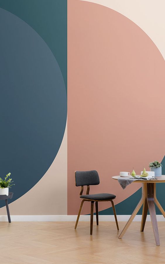 Modern dining area with geometric wall art, grey chair, wooden table, and plants in minimalist interior design.