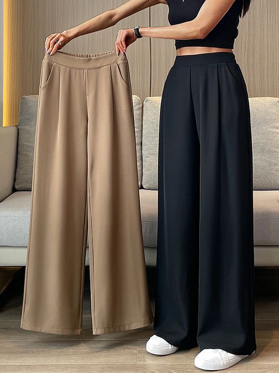 A woman wearing black wide-leg pants and holding beige wide-leg pants, showcasing trendy and comfortable fashion styles.