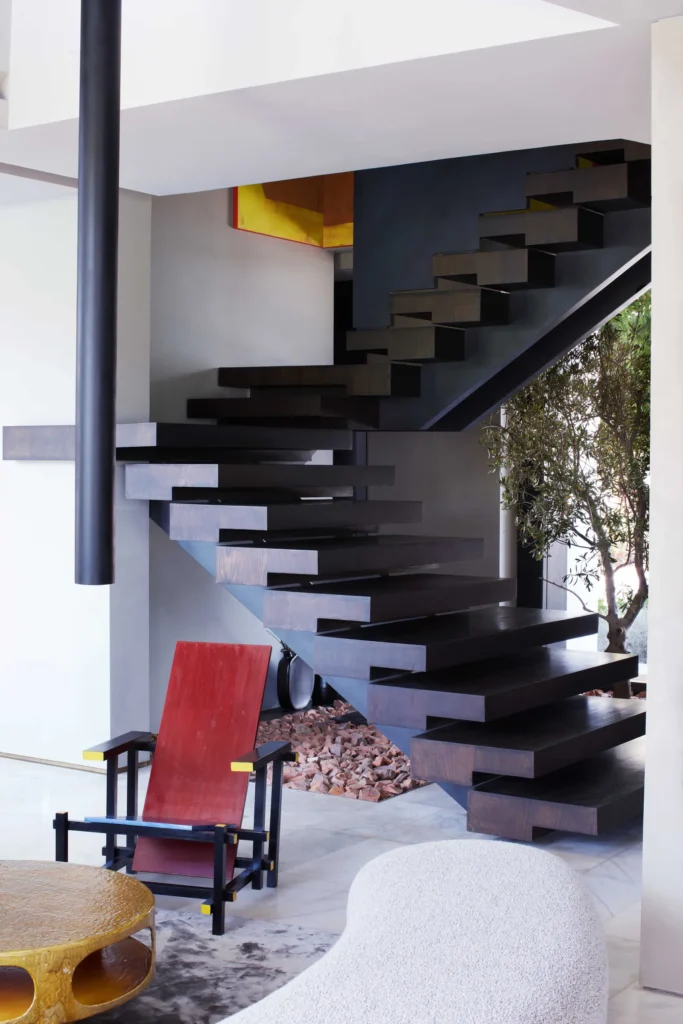 Modern interior with floating wooden staircase, red accent chair, and minimalist décor elements in contemporary home.