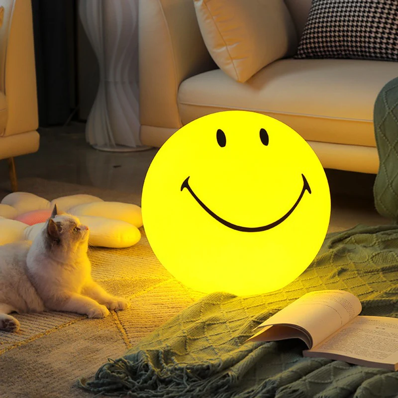 Cozy living room with a cat next to a glowing smiley face lamp on the floor, near a sofa and an open book.