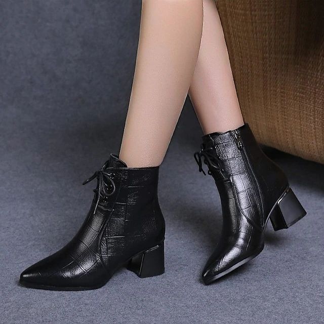 Black leather ankle boots with chunky heels and laces worn by a person with sheer tights, resting on a gray carpet.