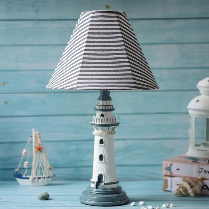 Nautical-themed lighthouse table lamp with striped shade on blue wooden background; maritime decor with books and boat.