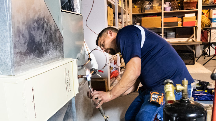 Technician repairing a furnace in a basement, surrounded by shelves with tools and storage boxes.