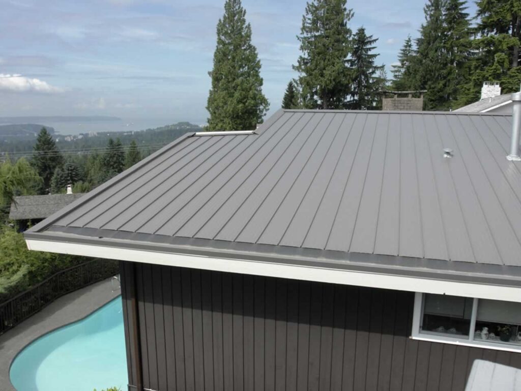 Modern metal roof on a house with a pool and scenic view of trees and distant mountains under a clear blue sky.