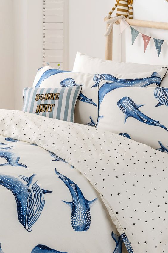 Whale-themed bedding with Bonne Nuit pillow, star-patterned sheets, and colorful bunting decoration in a cozy bedroom.