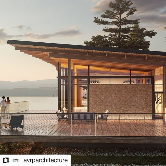 Modern lakefront house with glass walls, wooden deck, and scenic views. Evening sunlight enhances the serene atmosphere. #architecture