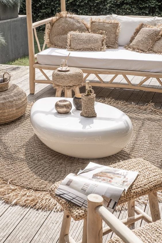 Boho outdoor patio with a white coffee table, wicker furniture, rattan pillows, and a magazine on a stool.