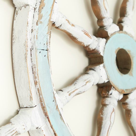 Close-up of a vintage ship wheel decoration with distressed white and blue paint, showcasing nautical home decor.