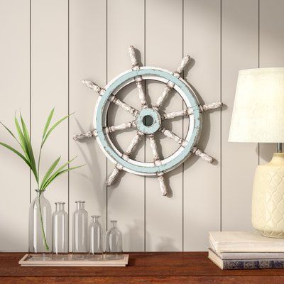 Nautical-themed decor with a ship wheel, plant vase and books on a wooden shelf, enhancing coastal interior style.