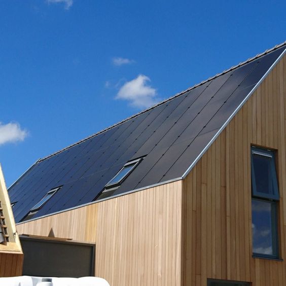 Modern wooden house with angled roof and skylights under a clear blue sky. Sustainable architecture and eco-friendly design.