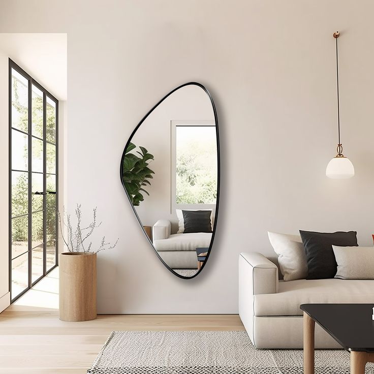 Modern living room with abstract mirror, white sofa, black pillows, hanging light, and large windows, well-lit and minimalistic.