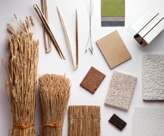 Eco-friendly construction materials including straw, wood shavings, wire, fabric samples, and insulation laid out on a table.