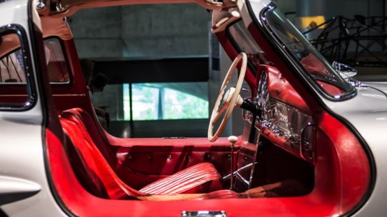 Classic car interior featuring red leather seats, a white steering wheel, and vintage dashboard controls.