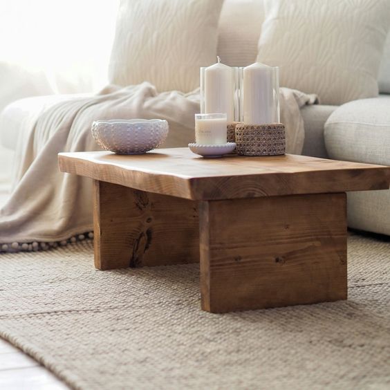 Rustic wooden coffee table with decorative candles and bowl on a beige rug in a cozy living room interior.