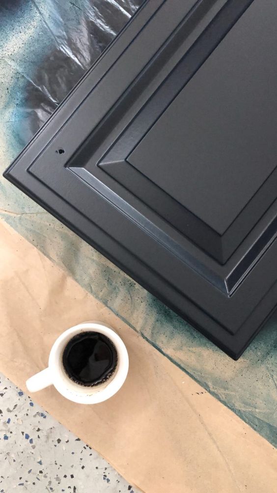 Cup of black coffee next to a freshly painted black cabinet door, displayed on a protective sheet.