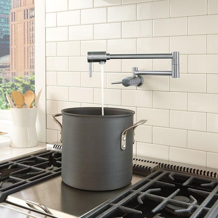 Wall-mounted pot filler faucet filling large pot on stove top in modern kitchen with white subway tile backsplash.